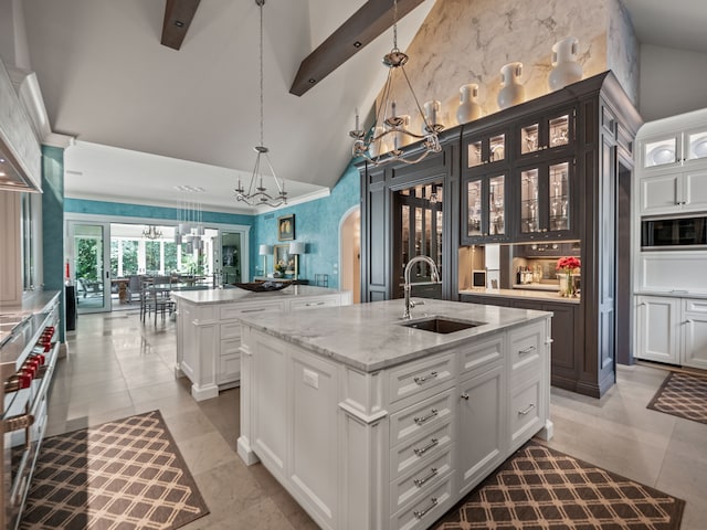 kitchen featuring sink, an island with sink, hanging light fixtures, light stone countertops, and beam ceiling