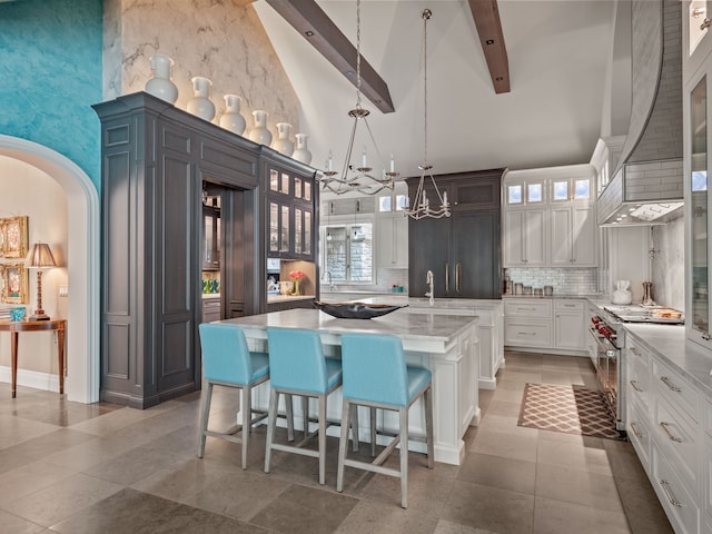 kitchen with a large island, hanging light fixtures, a towering ceiling, stainless steel stove, and beamed ceiling