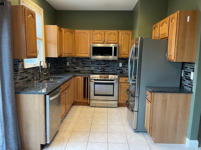 kitchen with sink, light tile patterned floors, appliances with stainless steel finishes, tasteful backsplash, and dark stone counters