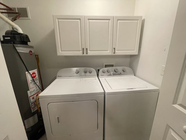 clothes washing area with cabinets, washer and clothes dryer, and water heater