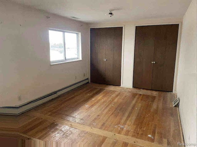 unfurnished bedroom featuring a baseboard radiator, hardwood / wood-style floors, and multiple closets