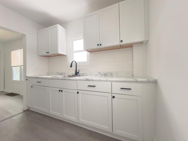 kitchen with light stone counters, white cabinets, backsplash, and sink