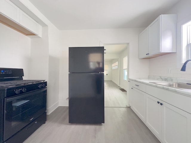 kitchen with black appliances, light wood-type flooring, decorative backsplash, sink, and white cabinetry