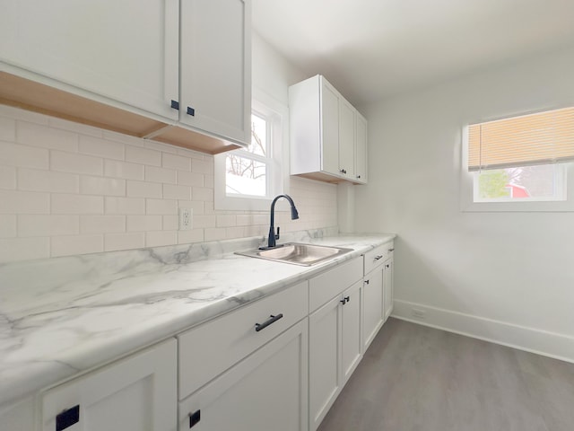 kitchen with light hardwood / wood-style floors, light stone counters, decorative backsplash, sink, and white cabinetry