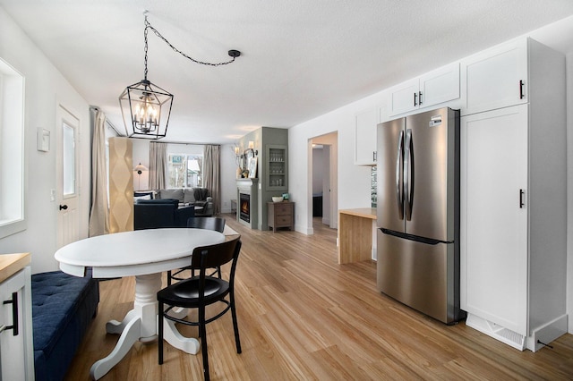 kitchen with white cabinetry, hanging light fixtures, light wood-type flooring, stainless steel fridge, and a notable chandelier