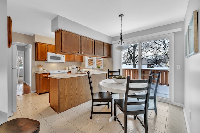 kitchen featuring white appliances, hanging light fixtures, a healthy amount of sunlight, and light tile patterned floors