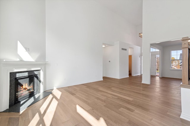 unfurnished living room featuring a towering ceiling, a premium fireplace, and light hardwood / wood-style floors