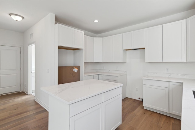 kitchen with white cabinets, light wood-type flooring, light stone countertops, and a center island