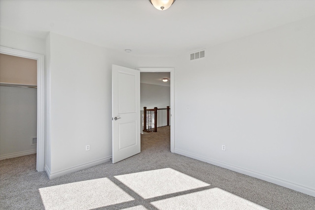 unfurnished bedroom with a spacious closet, a closet, and light carpet