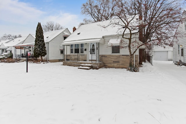 snow covered rear of property featuring a garage, an outdoor structure, and a porch