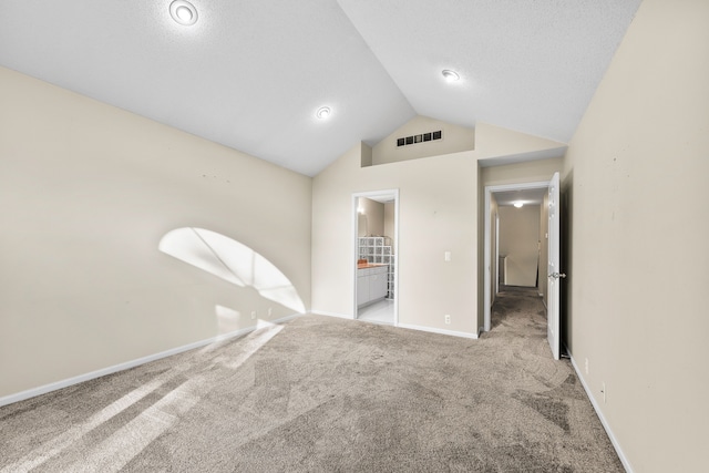 unfurnished room featuring light carpet, a textured ceiling, and vaulted ceiling