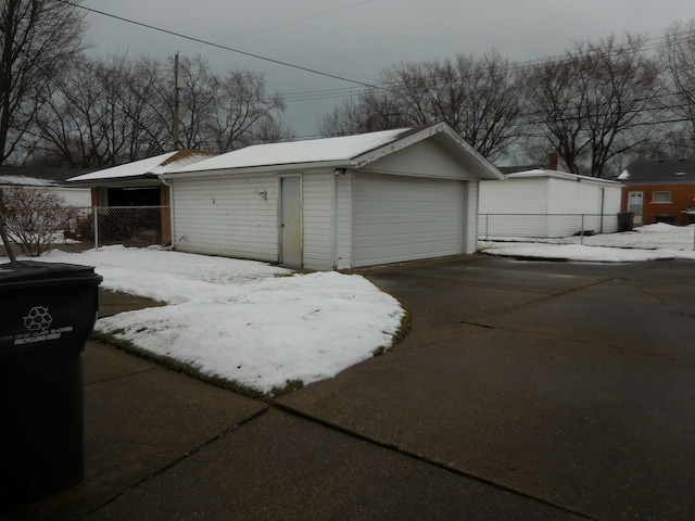 snow covered garage featuring a garage and fence