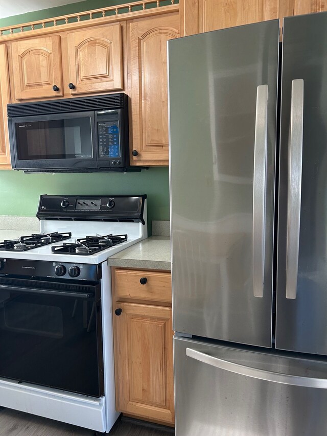 kitchen with light countertops, light brown cabinetry, freestanding refrigerator, gas range, and black microwave