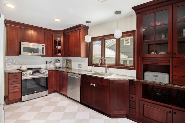 kitchen with decorative light fixtures, stainless steel appliances, light stone countertops, and sink