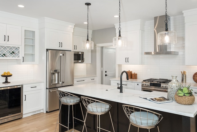 kitchen featuring stainless steel appliances, white cabinetry, light stone counters, wall chimney range hood, and wine cooler