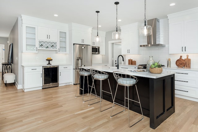 kitchen with beverage cooler, stainless steel appliances, white cabinets, light hardwood / wood-style flooring, and wall chimney range hood