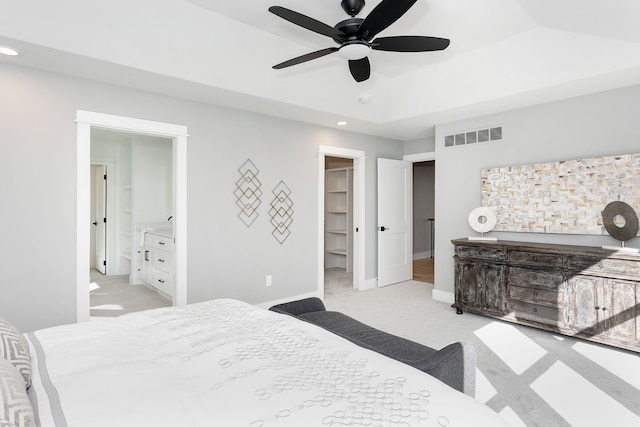 carpeted bedroom with ensuite bathroom, a raised ceiling, ceiling fan, a closet, and a walk in closet