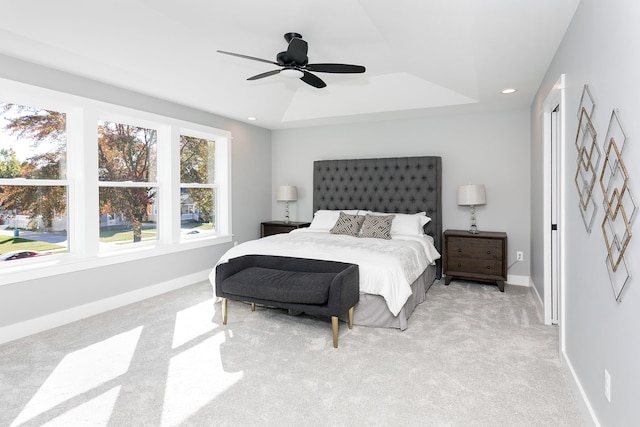 bedroom with ceiling fan, light colored carpet, and a tray ceiling