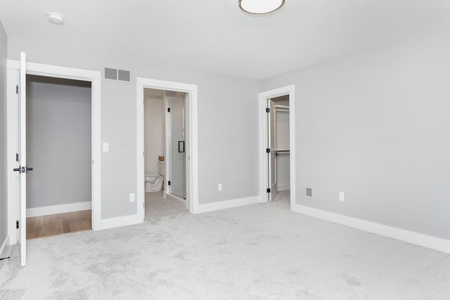 unfurnished bedroom with a walk in closet, ensuite bathroom, a closet, and light carpet