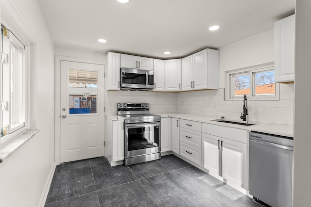 kitchen with appliances with stainless steel finishes, light stone countertops, sink, white cabinets, and tasteful backsplash