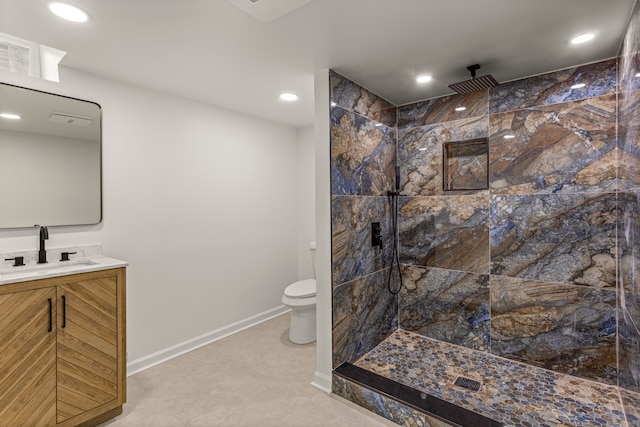 bathroom with toilet, tiled shower, and vanity