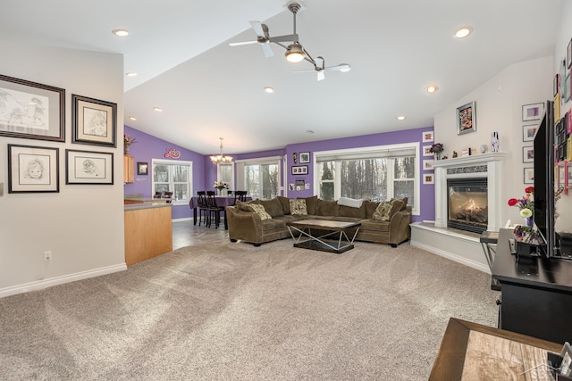 living room with ceiling fan with notable chandelier, a premium fireplace, carpet, and vaulted ceiling