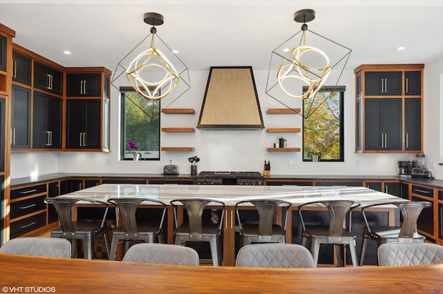 kitchen with custom exhaust hood, a kitchen island, a breakfast bar area, and hanging light fixtures