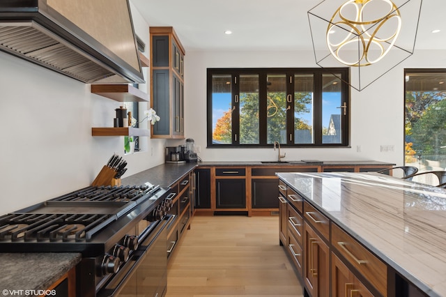 kitchen featuring pendant lighting, dark stone counters, light hardwood / wood-style floors, range with two ovens, and exhaust hood