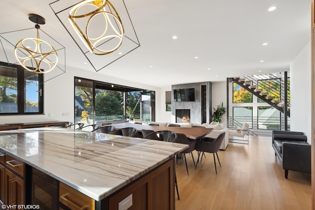 kitchen featuring a chandelier, light hardwood / wood-style flooring, pendant lighting, a premium fireplace, and light stone countertops