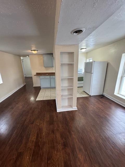 unfurnished living room with wood-type flooring, a textured ceiling, and built in shelves