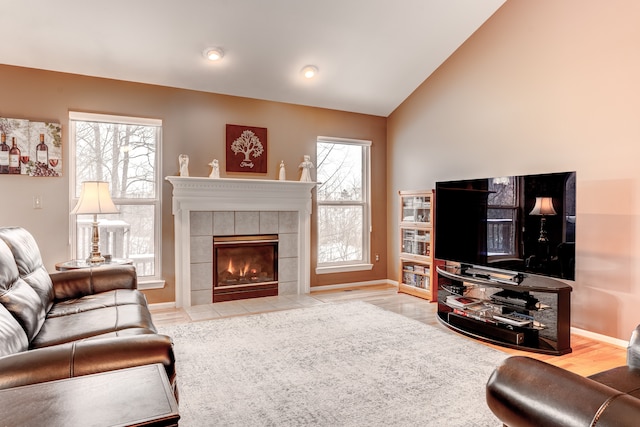 living room with a fireplace, a wealth of natural light, vaulted ceiling, and light hardwood / wood-style flooring