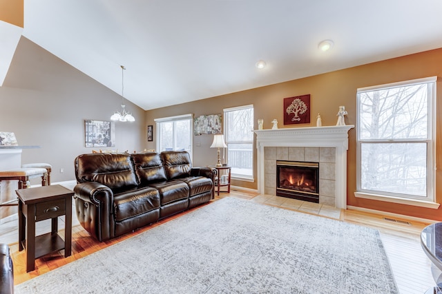 living room with wood-type flooring, a tiled fireplace, high vaulted ceiling, and a notable chandelier