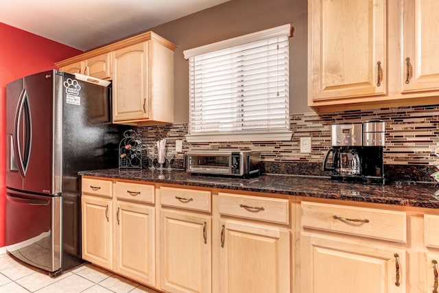 kitchen with stainless steel fridge with ice dispenser, light tile patterned floors, dark stone counters, light brown cabinets, and backsplash