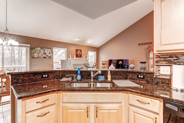 kitchen with dark stone countertops, vaulted ceiling, pendant lighting, sink, and an inviting chandelier