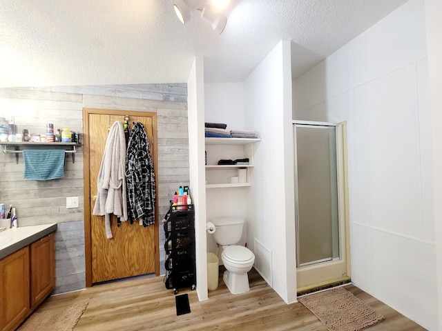 bathroom with hardwood / wood-style flooring, vaulted ceiling, wooden walls, a shower with door, and vanity