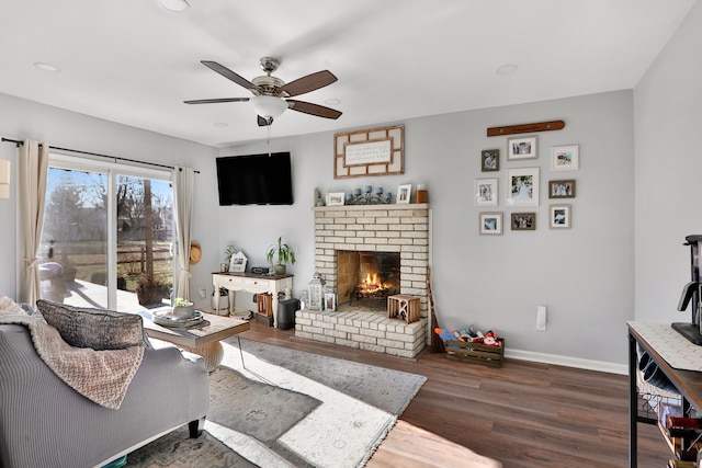 living room featuring dark wood-type flooring, ceiling fan, and a brick fireplace