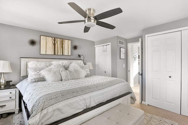 bedroom featuring ceiling fan, light colored carpet, and two closets