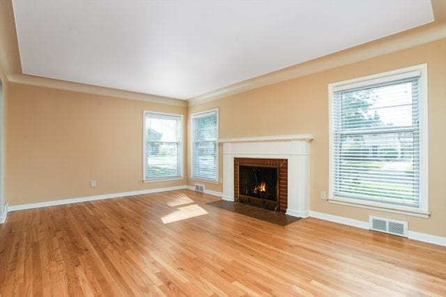 unfurnished living room featuring light hardwood / wood-style floors, ornamental molding, and a brick fireplace