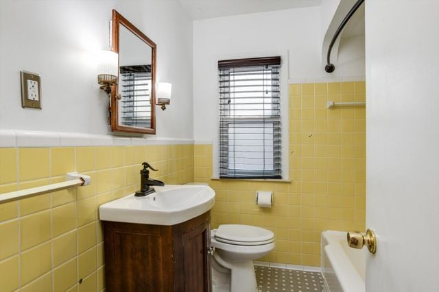 bathroom featuring toilet, a bathing tub, tile patterned flooring, tile walls, and vanity