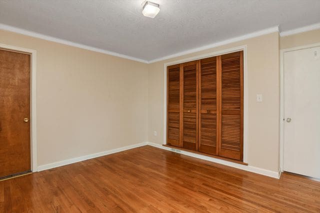 unfurnished bedroom with a closet, ornamental molding, and wood-type flooring