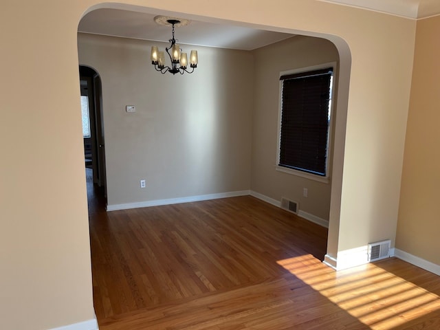 empty room with wood-type flooring and an inviting chandelier