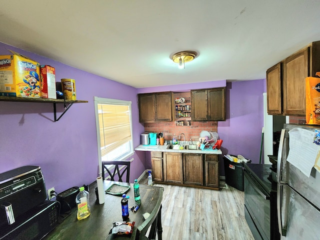 kitchen featuring stainless steel refrigerator, light wood-type flooring, decorative backsplash, sink, and black / electric stove