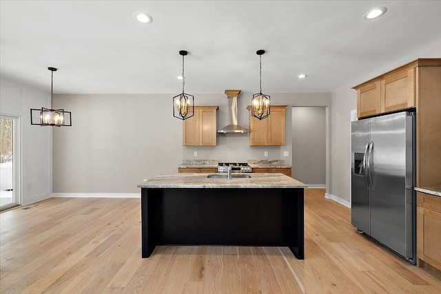 kitchen featuring light stone counters, hanging light fixtures, stainless steel fridge with ice dispenser, light hardwood / wood-style floors, and wall chimney range hood