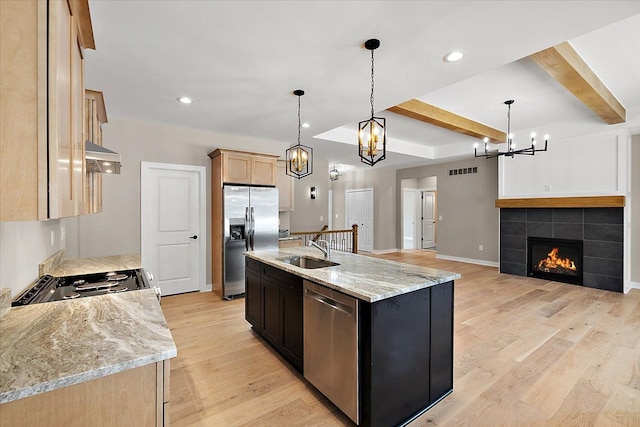 kitchen with hanging light fixtures, a center island with sink, a fireplace, appliances with stainless steel finishes, and sink