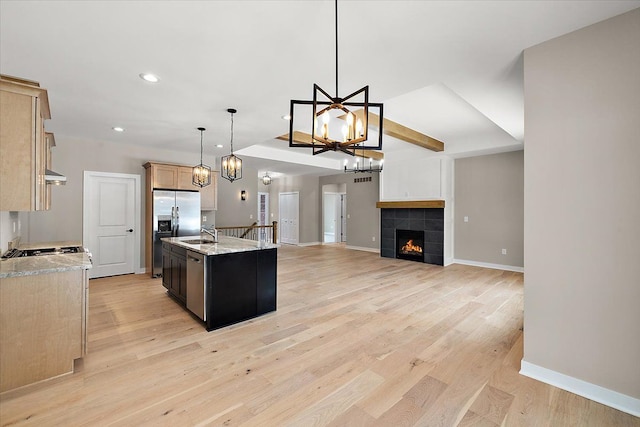 kitchen featuring light hardwood / wood-style flooring, hanging light fixtures, stainless steel fridge, a kitchen island with sink, and a fireplace