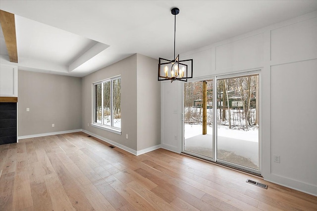 unfurnished dining area with light wood-type flooring, a raised ceiling, and an inviting chandelier