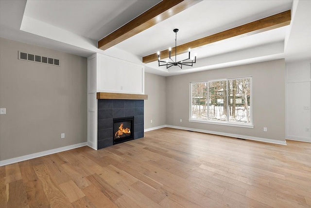 unfurnished living room featuring a tiled fireplace, light hardwood / wood-style flooring, and a notable chandelier