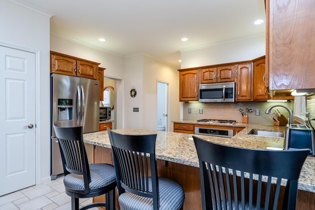 kitchen featuring sink, light stone counters, a breakfast bar area, backsplash, and appliances with stainless steel finishes