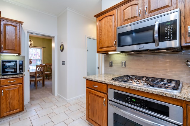 kitchen featuring stainless steel appliances, light stone counters, backsplash, crown molding, and a notable chandelier