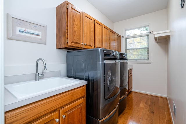 washroom with sink, washing machine and clothes dryer, hardwood / wood-style flooring, and cabinets